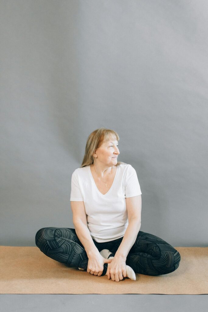 A senior woman sits cross-legged on a mat, engaging in a yoga session for relaxation and wellness.