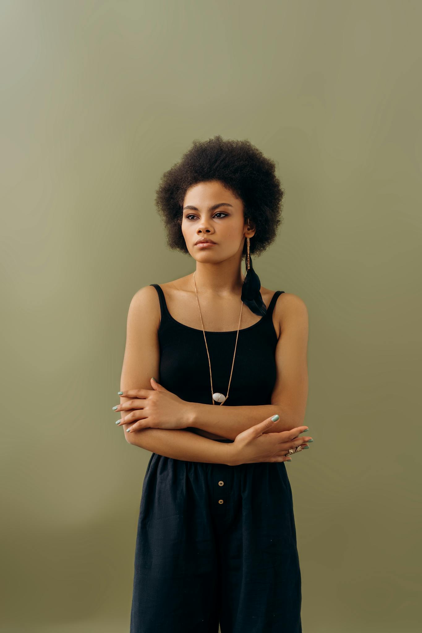 Confident woman with afro hairstyle in black outfit posing against a plain background.